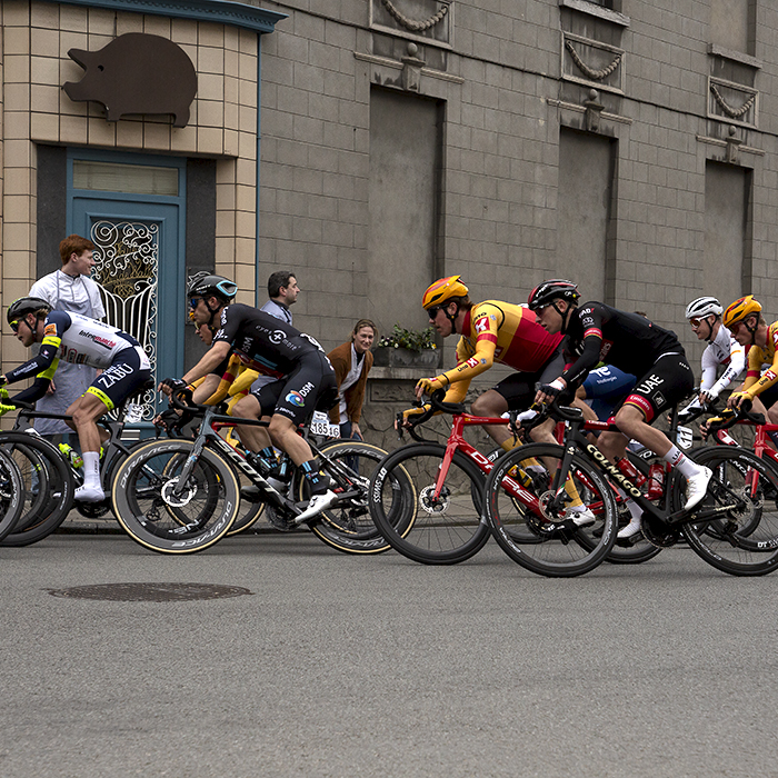 Dwars Door Vlaanderen 2022 - The main group go past a butcher’s shop with an ornate door