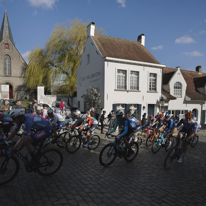 Dwars Door Vlaanderen 2024 - Riders pass through the main square in Nokere, white washed buildings and a church behind them