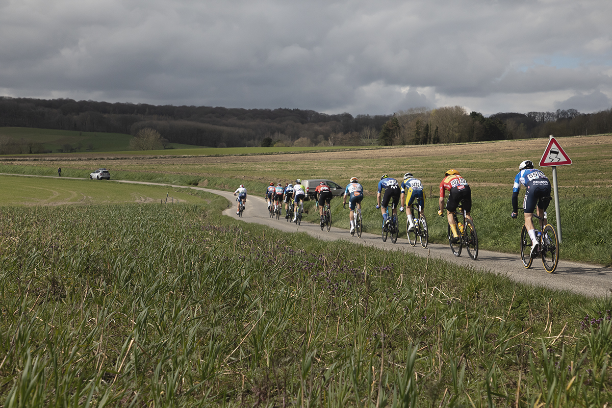 Dwars Door Vlaanderen 2024 - Riders pass by a slippery road sign on Rue des Chapelles
