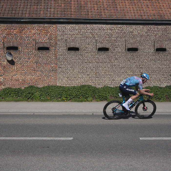 Dwars Door Vlaanderen 2025 - Mike Teunissen rides past the side of a brick built barn