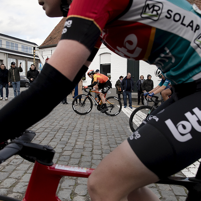 Dwars Door Vlaanderen Vrouwen 2024 - A rider is framed through the form of another as they climb Nokereberg