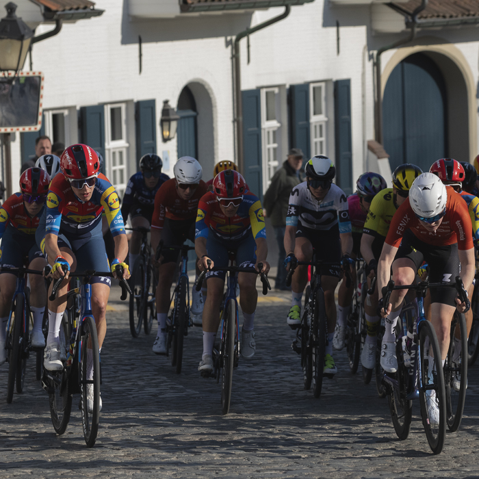 Dwars Door Vlaanderen Vrouwen 2025 - Riders pass white washed buildings in the village of Nokere