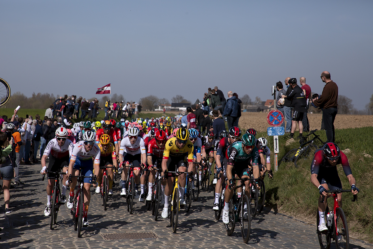 E3 Saxo Bank Classic 2022 - Fans line banks and a Latvian flag is flown as the peloton makes its way down Holleweg