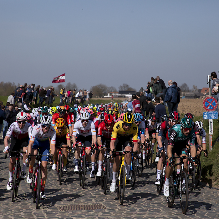 E3 Saxo Bank Classic 2022 - Fans line banks and a Latvian flag is flown as the peloton makes its way down Holleweg