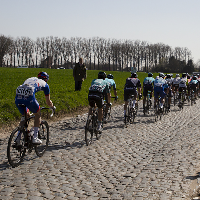 E3 BinckBank Classic 2019 - A fan watches the last riders in the peloton pass by as they ride down the cobbled Holloweg