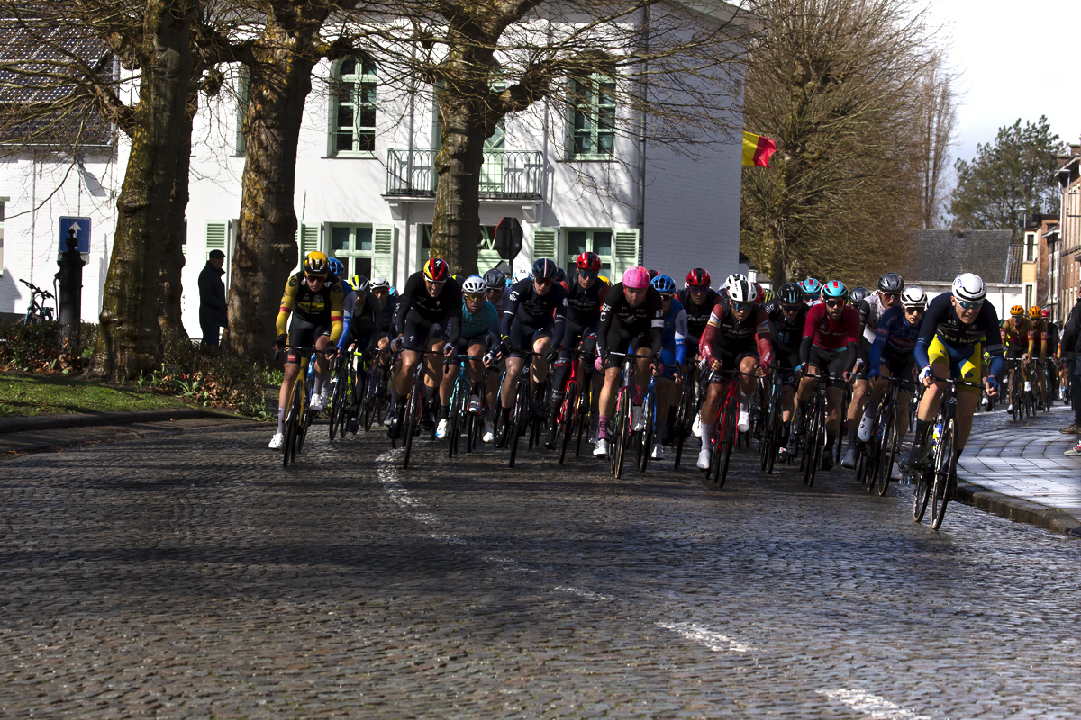 E3 Saxo Classic 2023 -The peloton on a cobbled road moves through a small town