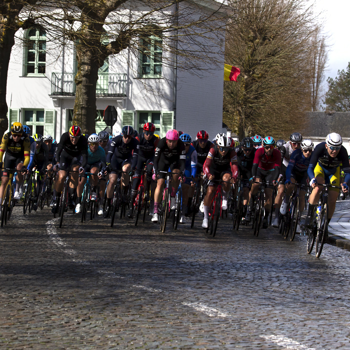 E3 Saxo Classic 2023 -The peloton on a cobbled road moves through a small town