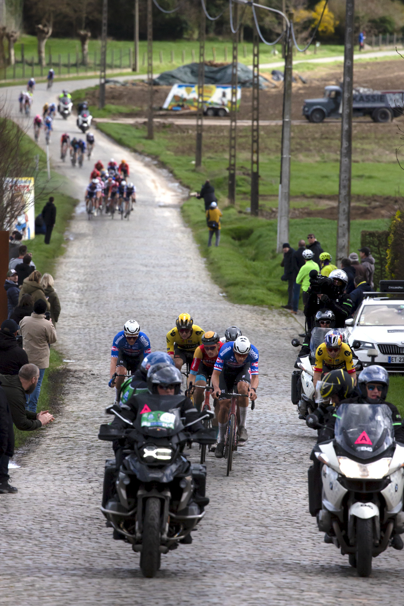 E3 Saxo Classic 2023 - An elite breakaway group makes its way up the cobbles preceded by motorbikes