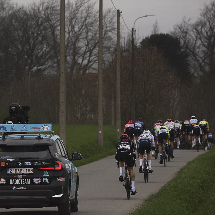 E3 Saxo Classic 2024 - A group of riders are followed by a race vehicle