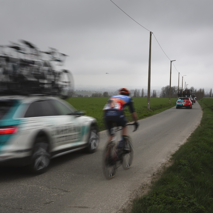 E3 Saxo Classic 2024 - A rider in the convoy of team cars speeds down Langekouter
