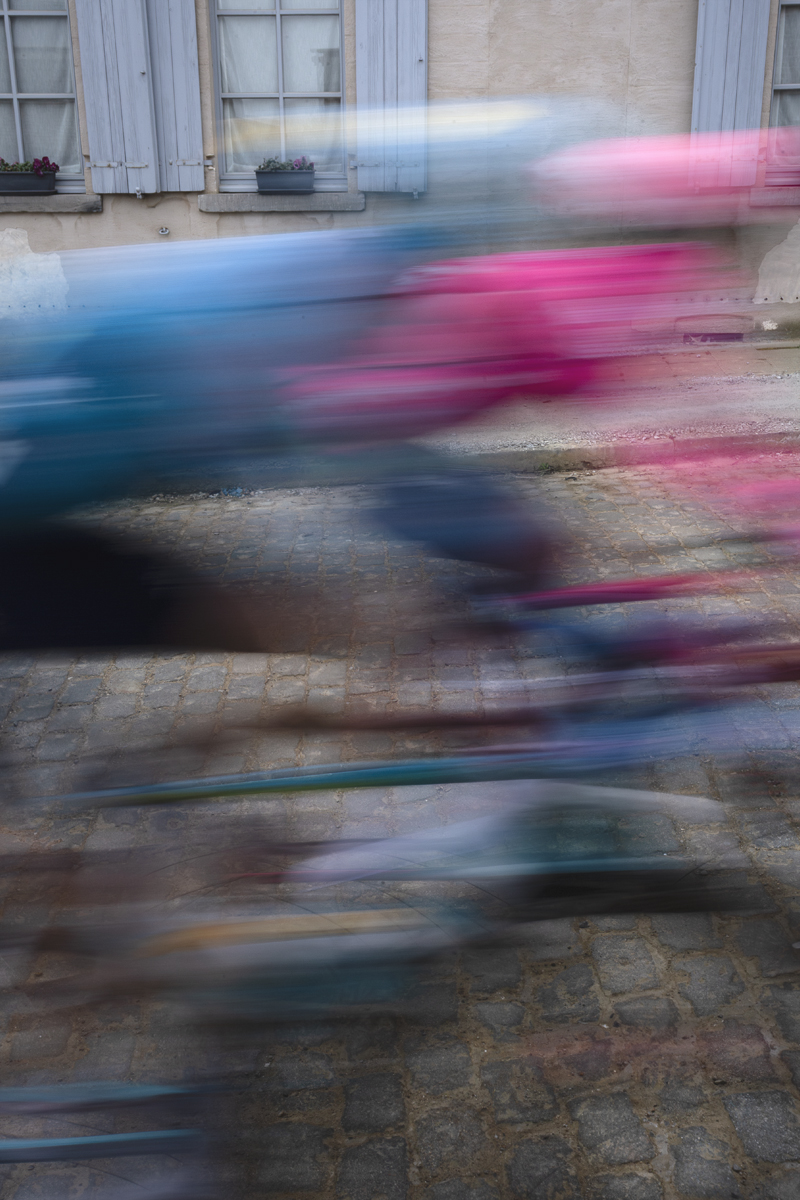 E3 Saxo Classic 2025 - Riders speed past a traditional building with blue shutters as they begin the Stationberg climb