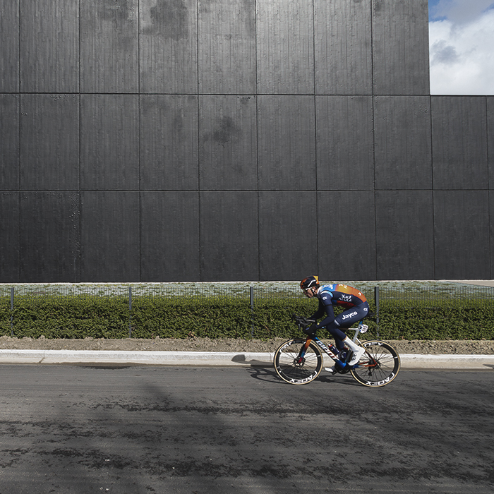 Gent Wevelgem 2024 - A rider passes in front of a large black warehouse in Morsele