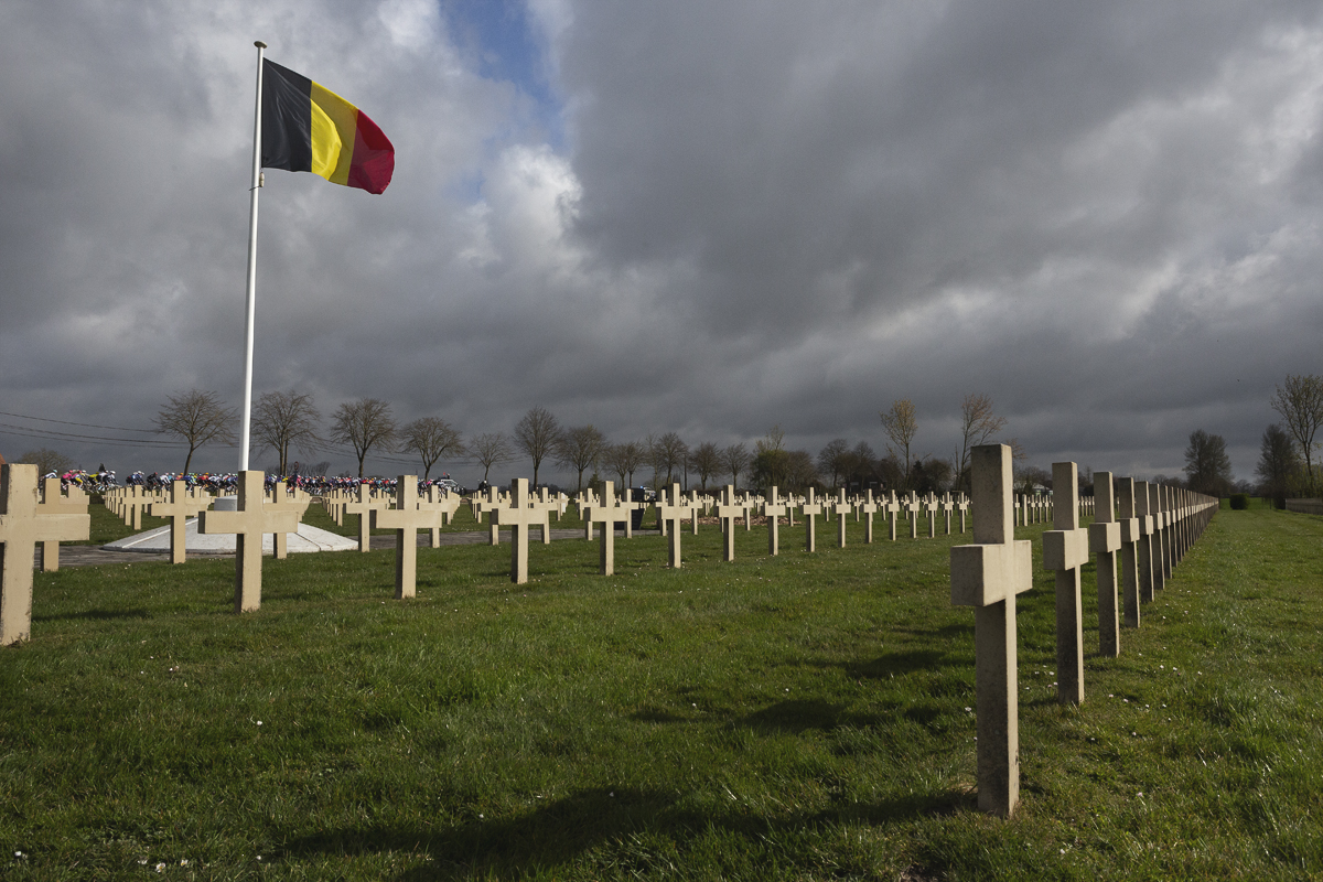 Gent Wevelgem 2025 - The race passes in front of Saint-Charles de Potyze cemetery with graves marked with lines of crosses while a Belgian flag flaps above