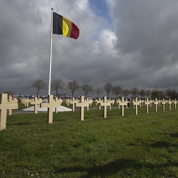 Gent Wevelgem 2025 - The race passes in front of Saint-Charles de Potyze cemetery with graves marked with lines of crosses while a Belgian flag flaps above
