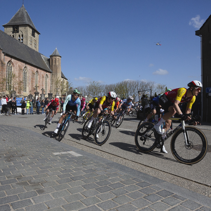 Gent Wevelgem 2025 - The peloton takes a corner with the church of Sint Vedastuskerk in the background