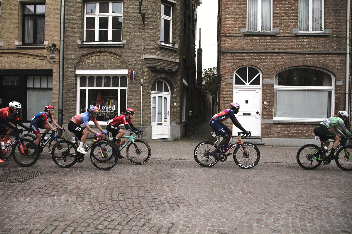Gent Wevelgem Vrouwen 2024 - Riders from the side as they pass by the facades of tall brick buildings inIeper / Ypres