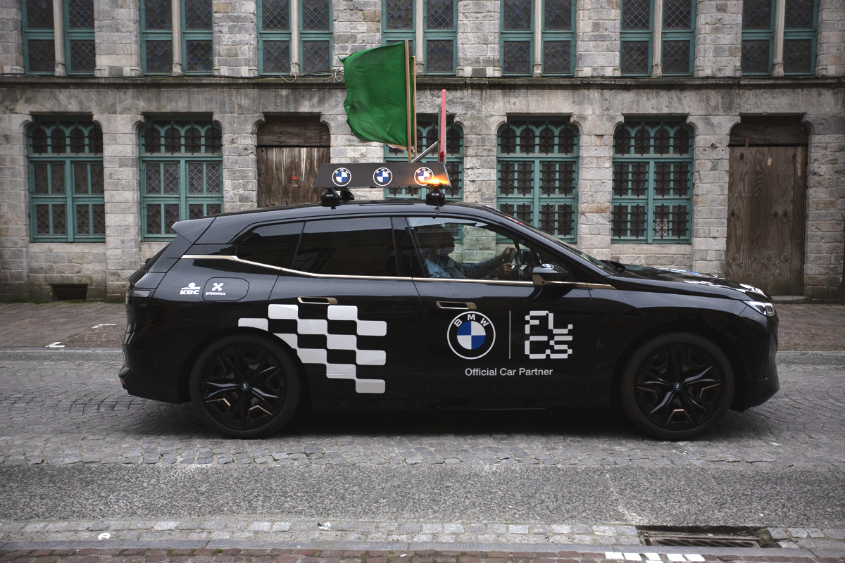 Gent Wevelgem Vrouwen 2024 - A Flanders Classic branded car with a green flag flying from its roof signals the passage of the race