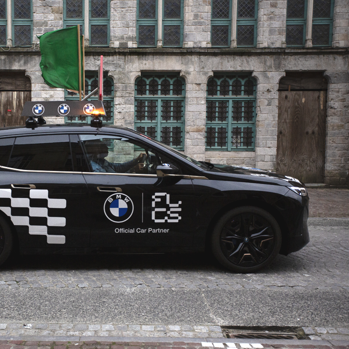 Gent Wevelgem Vrouwen 2024 - A Flanders Classic branded car with a green flag flying from its roof signals the passage of the race