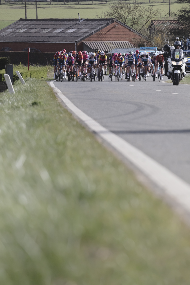 Gent Wevelgem Vrouwen 2025 - Riders approach with old farm buildings behind them in Loker