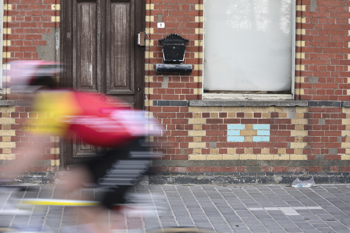 Gent Wevelgem Vrouwen 2025 - A Cofidis rider speeds past an old brick building in Reningelst