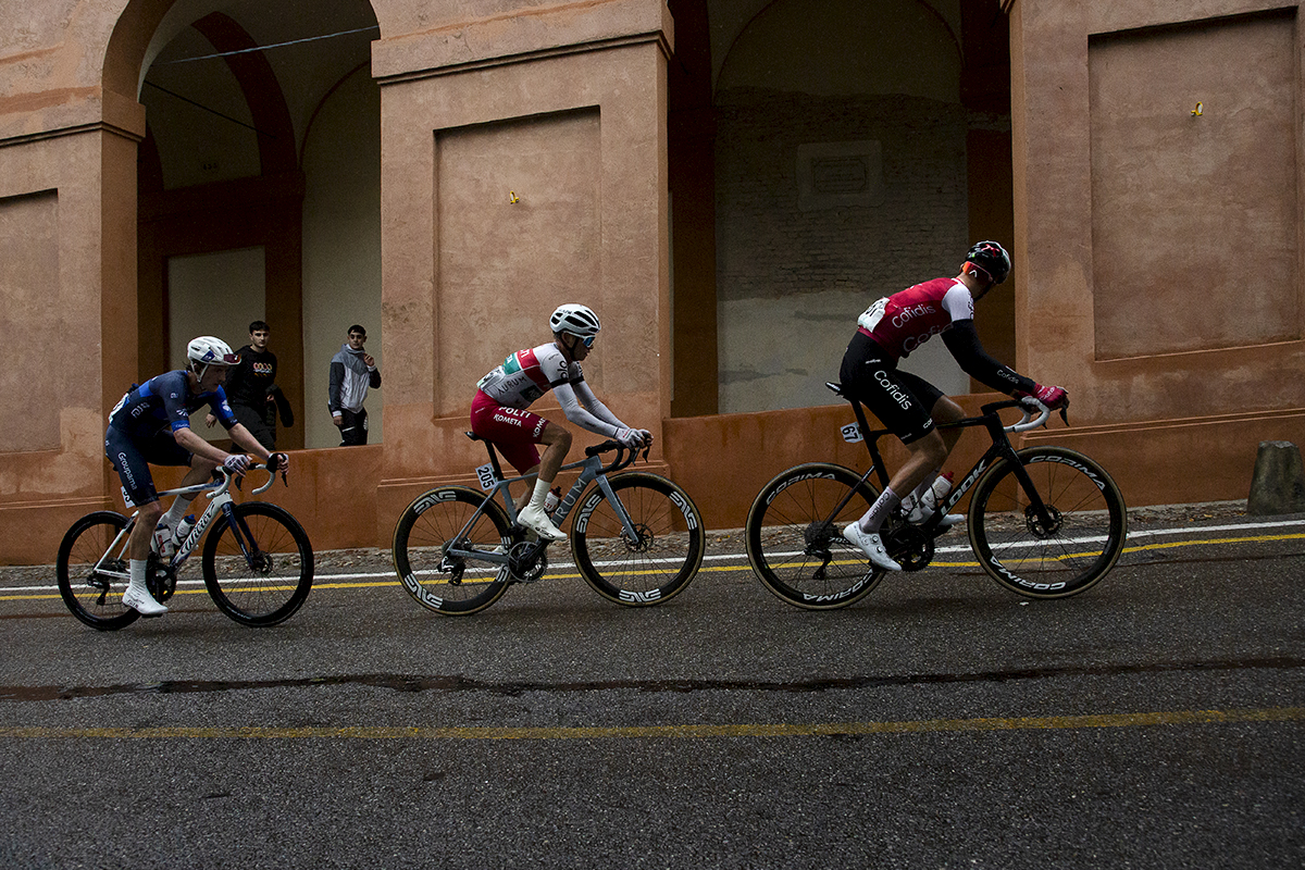 Giro dell’Emilia 2024 - A group of three riders ride past the terracotta portico on Via di San Luca