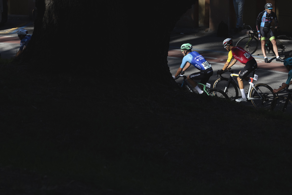 Giro dell’Emilia 2025 - Riders are lit by strong sunlight as they are framed by a tree in deep shadow in Bologna