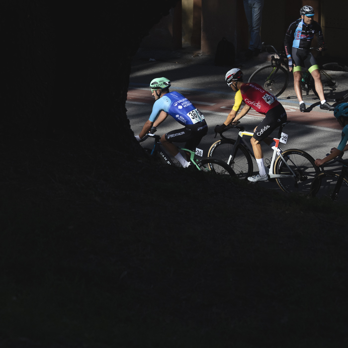 Giro dell’Emilia 2025 - Riders are lit by strong sunlight as they are framed by a tree in deep shadow in Bologna