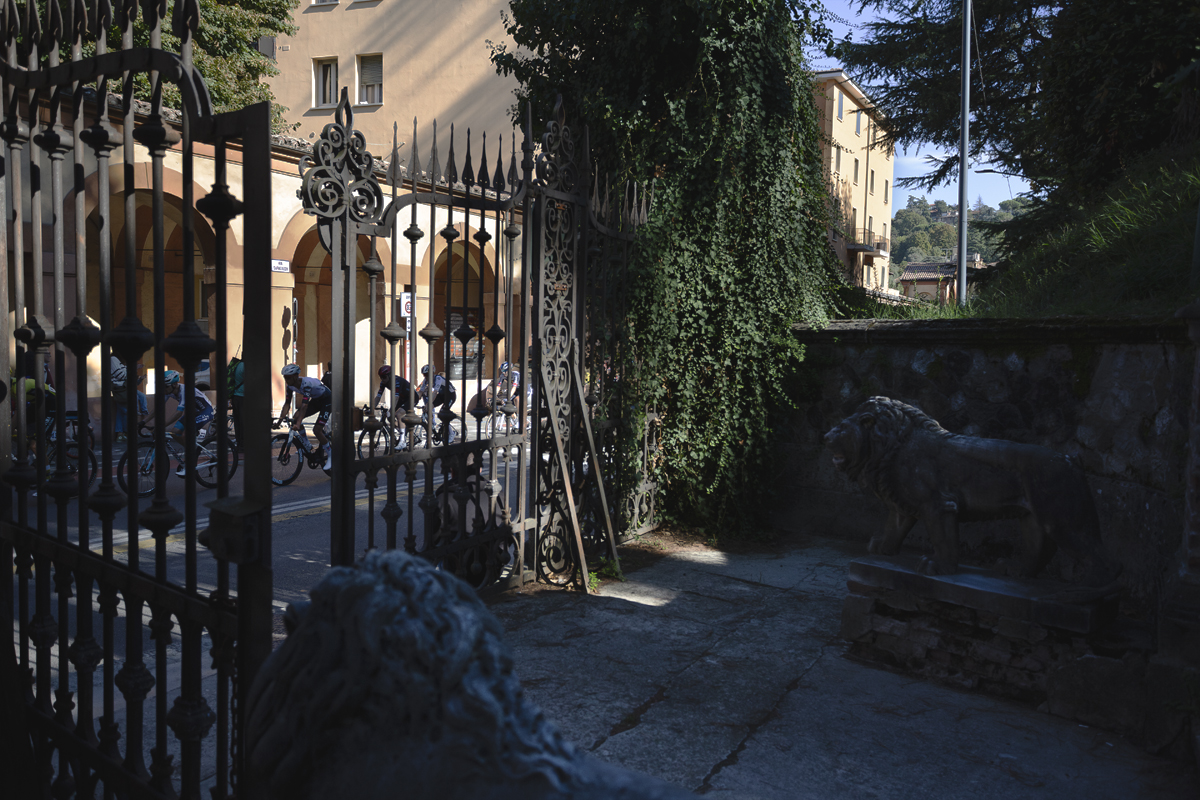 Giro dell’Emilia 2025 - Riders pass by ornate gates flanked by lion sculptures in Bologna