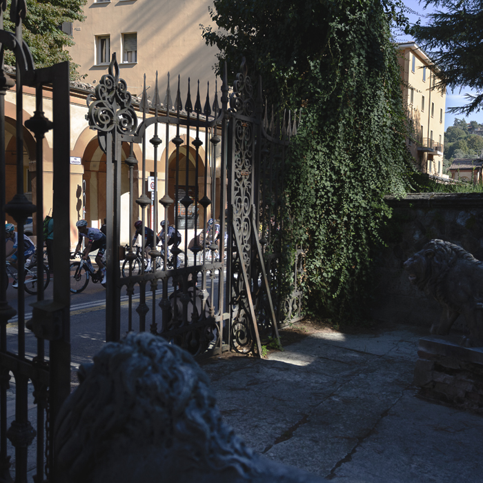 Giro dell’Emilia 2025 - Riders pass by ornate gates flanked by lion sculptures in Bologna
