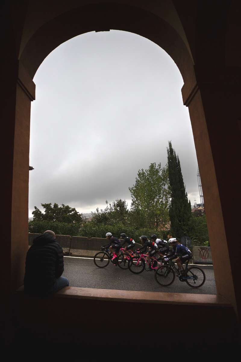 Giro dell'Emilia Internazionale Donne Elite 2024 - A fan sits in an archway in the portico watching a group of riders on the Via di San Luca