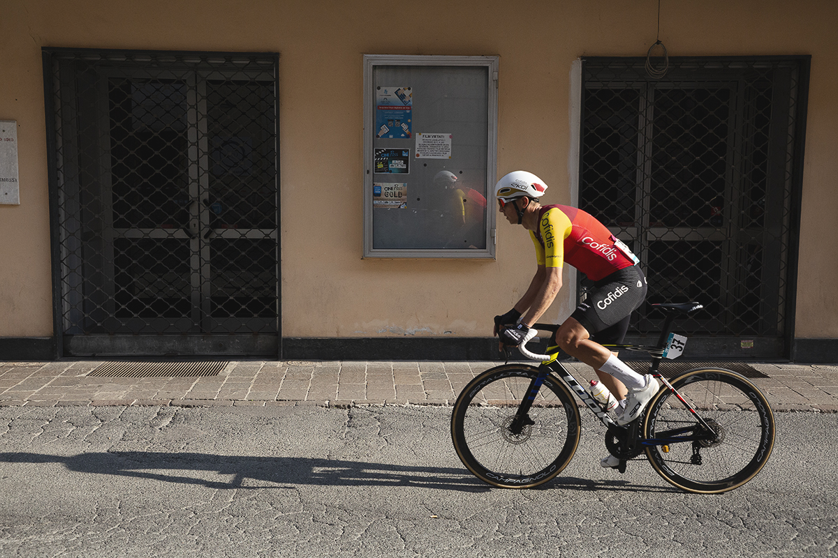 Gran Piemonte 2025 - Dylan Teuns casts a long shadow as he rides past a small cinema in Acqui Terme