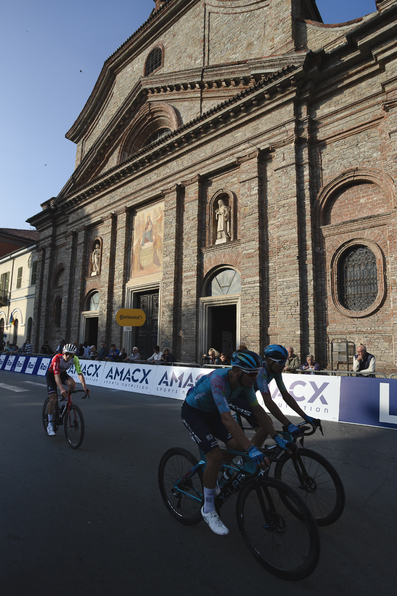Gran Piemonte 2025 - Riders pass the Parrocchia di San Francesco which is lit by the late afternoon sun