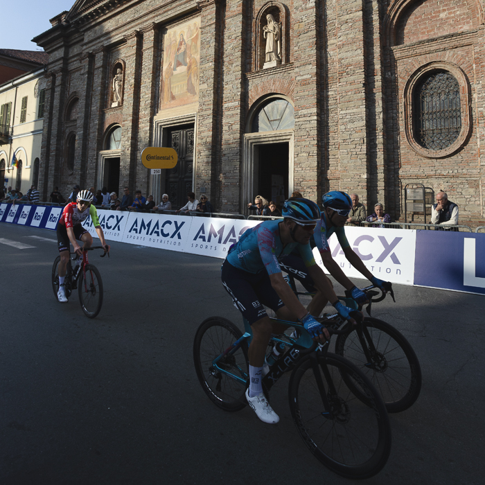 Gran Piemonte 2025 - Riders pass the Parrocchia di San Francesco which is lit by the late afternoon sun