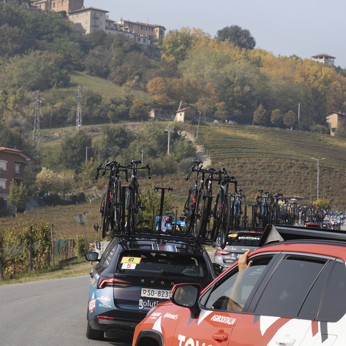 Gran Piemonte 2025 - The race convoy rounds a corner with trees beginning to show their autumnal colours in the distance