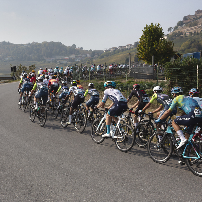 Gran Piemonte 2025 - The peloton rounds a corner with a hill village seen in the distance