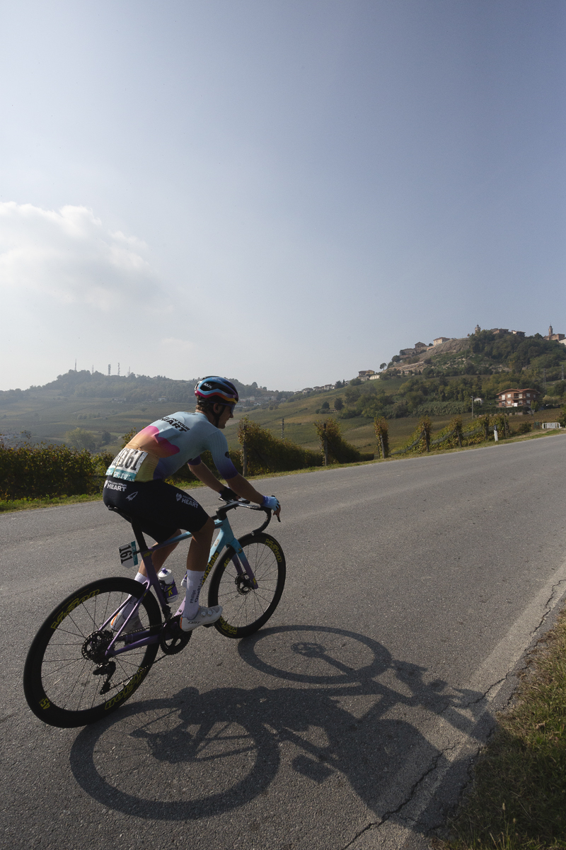 Gran Piemonte 2025 - Cedrik Bakke Christophersen passes through fields of vines with a hill village in the distance