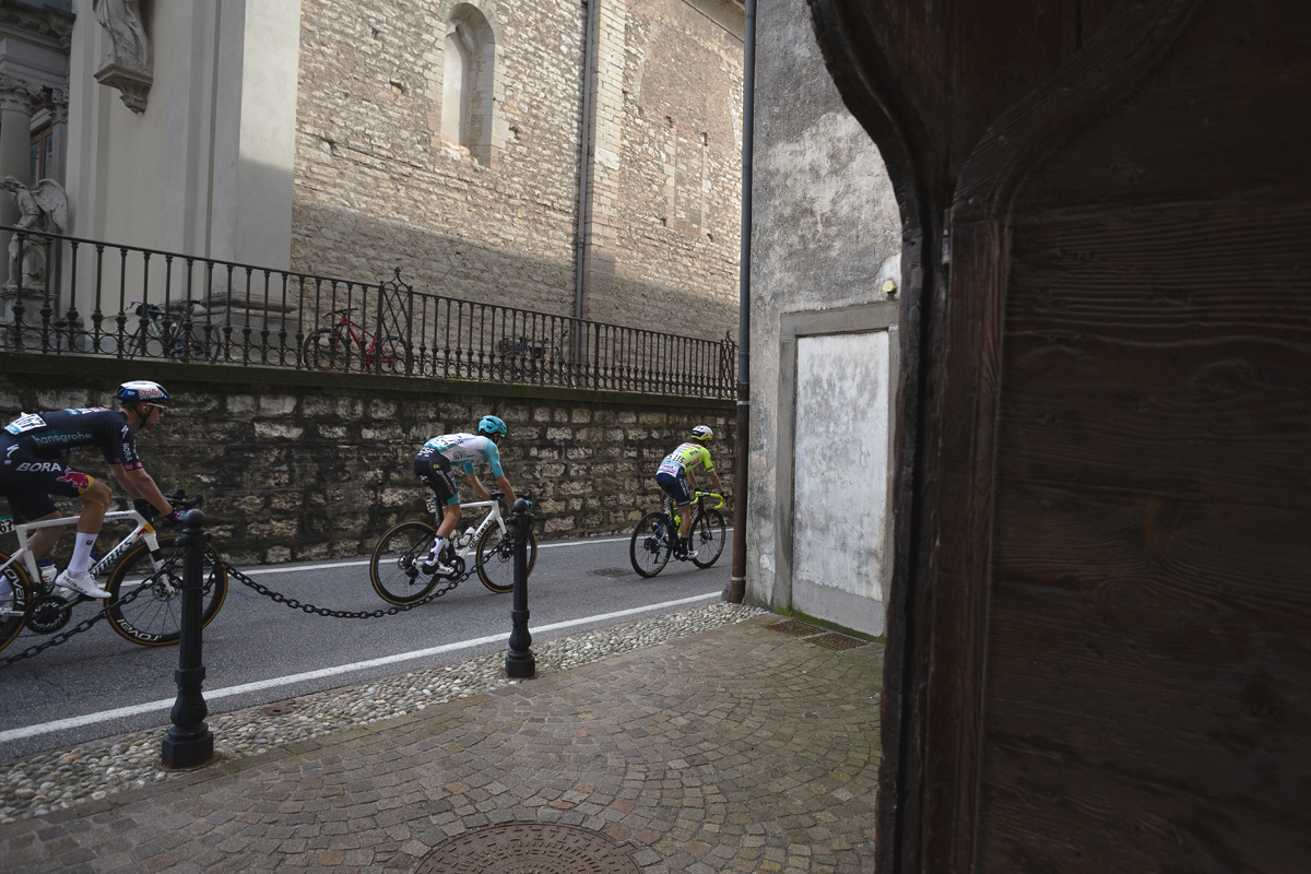 Il Lombardia 2024 - Riders seen through the door of a small courtyard in Almenno San Salvatore