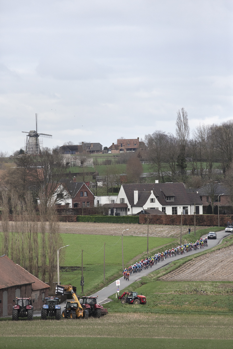 Kuurne Brussel Kuurne 2024 - Riders seen from the distance with a windmill in the background as they come onto Beerbosstraat