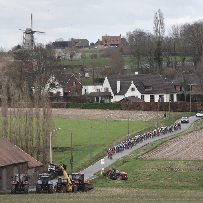 Kuurne Brussel Kuurne 2024 - Riders seen from the distance with a windmill in the background as they come onto Beerbosstraat