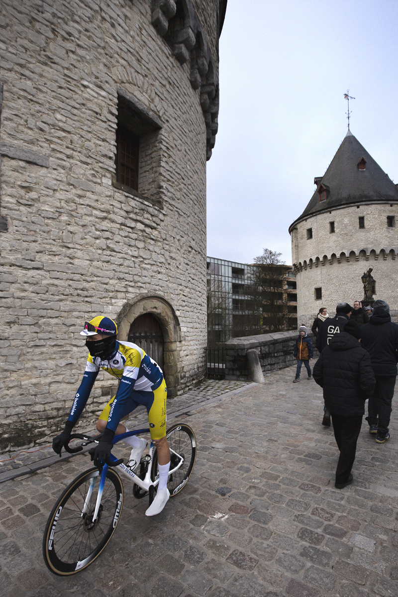 Kuurne Brussel Kuurne 2024 - Alex Colman with a snood pulled up over his face cycles near the Broeltorens in Kortrijk