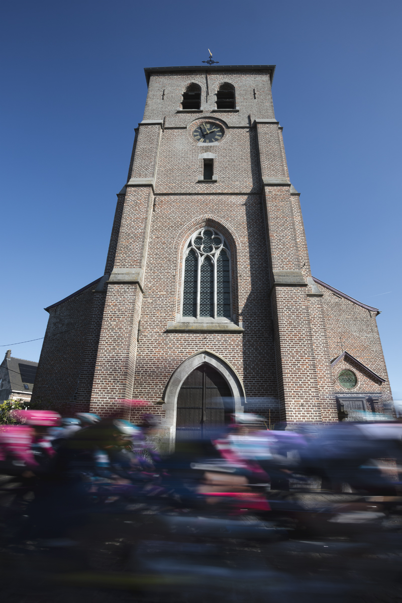 Kuurne Brussel Kuurne 2025 - The peloton speeds past the tower of a church in Etikove