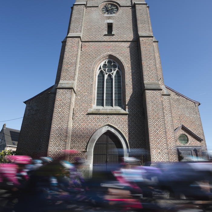 Kuurne Brussel Kuurne 2025 - The peloton speeds past the tower of a church in Etikove