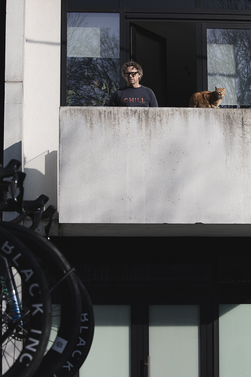 Kuurne Brussel Kuurne 2025 - A cat and its human survey the race cars from their balcony as they arrive in Kortrijk