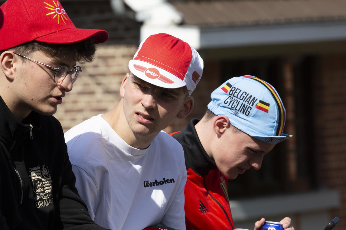 La Flèche Wallonne 2023 - A group of young people in cycling caps sit on a wall waiting for the race