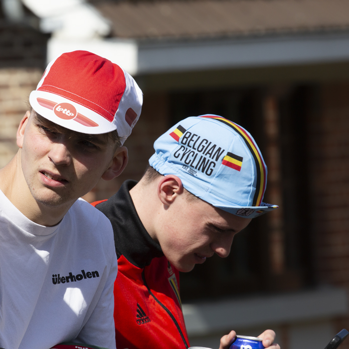 La Flèche Wallonne 2023 - A group of young people in cycling caps sit on a wall waiting for the race