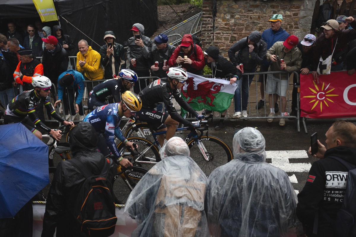 La Flèche Wallonne 2025 - The peloton passes supporters waving a Welsh flag on the Mur de Huy
