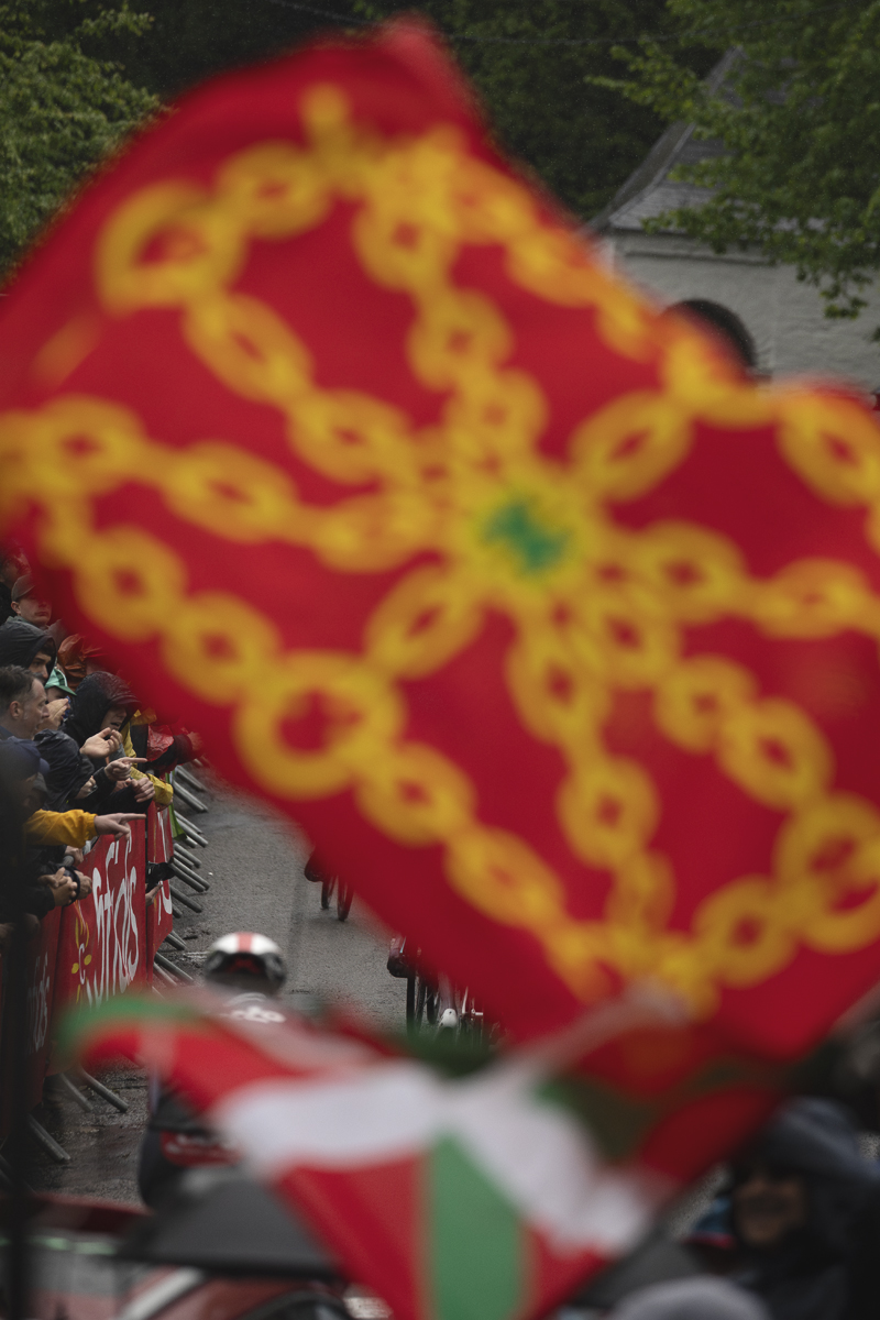 La Flèche Wallonne 2025 - Riders seen through flags being waved on the Mur de Huy