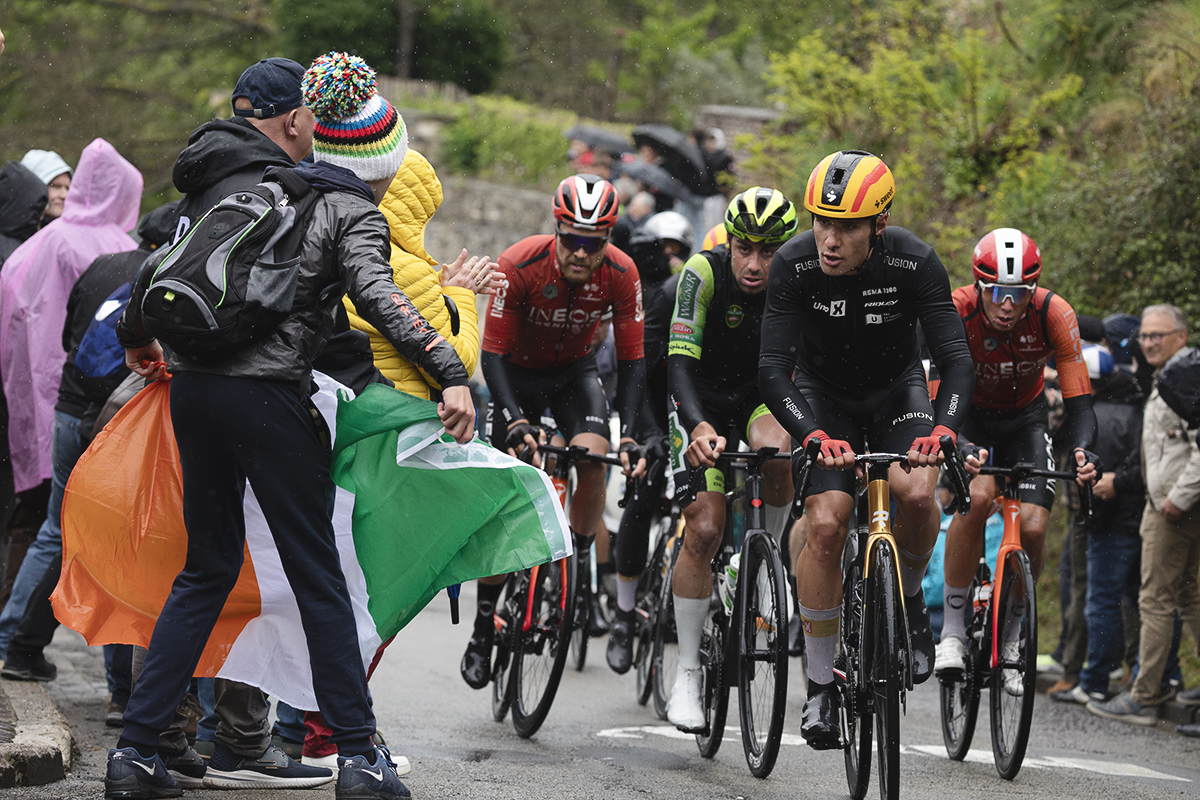 La Flèche Wallonne 2025 - A rider waves an Irish flag as riders pass on the Mur de Huy