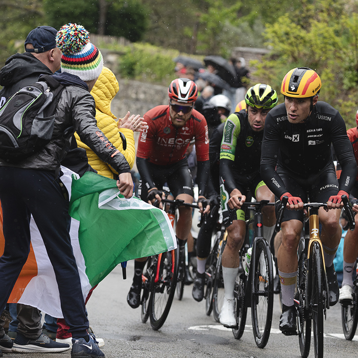 La Flèche Wallonne 2025 - A rider waves an Irish flag as riders pass on the Mur de Huy