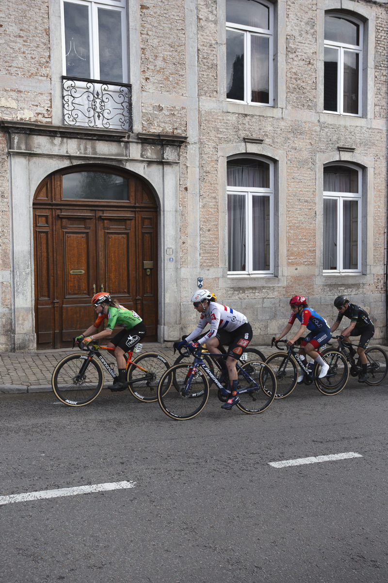 La Flèche Wallonne Femmes 2025 - Riders pass the large arched wooden door of a grand building in Huy